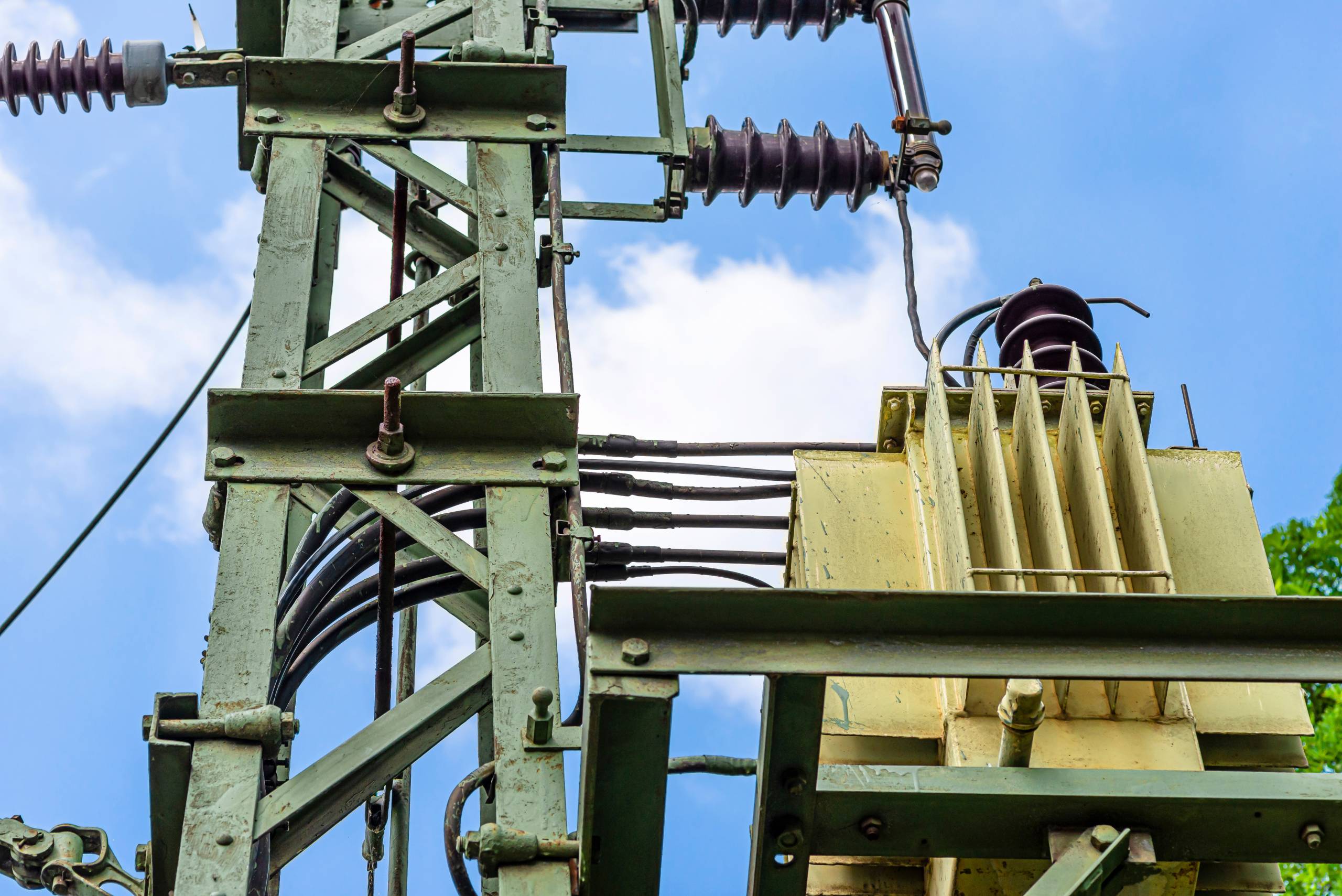 Green electric pole with a transformer standing next to railway tracks, used to distribute voltage on railway lines.